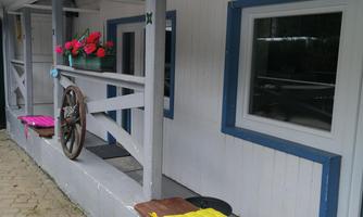 A cozy porch with colorful cushions and floral decorations. The walls are white with blue accents, and the floor is made of stones.