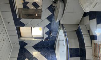 A modern bathroom with blue and white tiles. There is a shower, a bathtub, and an elegant sink.