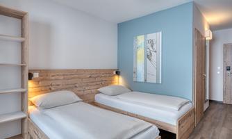 A modern bedroom with two wooden single beds. The walls are bright, and the room feels friendly and inviting.