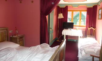 A cozy room with pink walls and two beds. A television stands on a table next to a window.