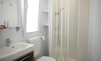 A modern bathroom with a shower and white walls. It includes a sink, a toilet, and a window for daylight.