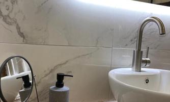 A stylish bathroom with a modern sink faucet and a large mirror. A towel and grooming products are on the floor.
