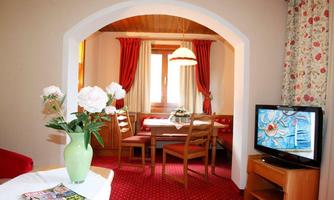A cozy room with a dining table and chairs. Red curtains hang at the window, and a vase with flowers is on the table.