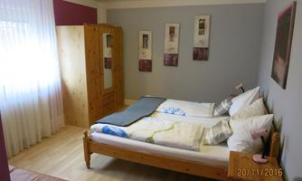 A simple and cozy bedroom with two beds. The room is bright and furnished with wooden furniture as well as decorative pictures on the walls.