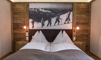 A cozy bedroom with a double bed and wood paneling. A picture of hikers in the mountains hangs on the wall.