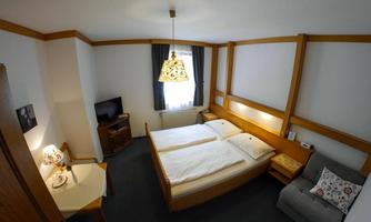 A cozy bedroom with two beds and bright, friendly colors. The room is equipped with a television, a table, and a comfortable armchair.