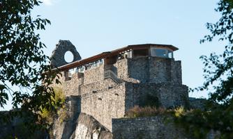 An old ruin on a hill, surrounded by trees. The sky is blue and clear.