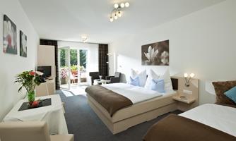 A modern hotel room with two beds, a small table, and a balcony. The room is bright and cheerful, decorated with fresh flowers in the foreground.
