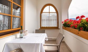 A cozy balcony with a table and two chairs. Colorful flowers are on the windowsill, creating an inviting atmosphere.