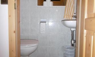 A small bathroom with bright tiles. There is a toilet, a sink, and a window with a towel.