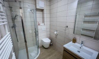 A modern bathroom with a shower and a sink. The walls are tiled in light colors and there is ample storage space.