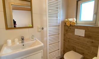 A bright bathroom with a wooden ceiling and modern fixtures. A sink, toilet, and towels are well arranged.