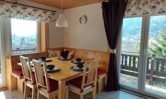 A cozy dining area with a large wooden table and chairs. The windows offer a lovely view of the surroundings.