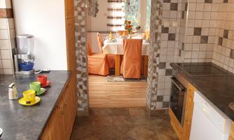 A modern kitchen with wooden cabinets and a view of an elegant dining area. The floor is designed with earth-tone tiles.