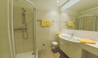 A modern bathroom with a shower and a sink. Yellow towels and a bright, inviting atmosphere create coziness.