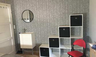 A modern room with a shelf and a sink. A round mirror hangs on the wall and a red chair stands next to it.