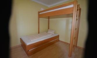 A simple bedroom with a wooden loft bed. Below it is a single bed, and the walls are painted in light yellow.