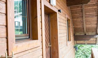 An entrance to a wooden house with a window and a front door. The floor is tiled and there is a small foyer.