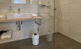 Bathroom with modern tiles and a walk-in shower. On the shelf are towels and a sink.