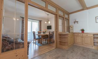 A bright and cheerful apartment with wooden details. The image shows a dining area with a table and chairs as well as a cozy living area.