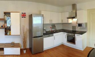 A modern kitchen with white cabinets and an elegant gray countertop. The kitchen is bright and well-organized, with wooden details and a refrigerator.