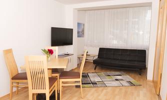 A modern living room with a table, chairs, and a television. A black sofa and a rug create a cozy atmosphere.