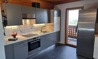A modern kitchen with gray cabinets and bright surfaces. A window offers a view of a balcony and the surroundings.