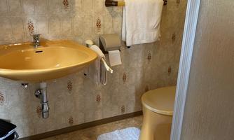 A bathroom with a yellow sink and toilet. The walls are decorated with a floral pattern and there is a shower cubicle.