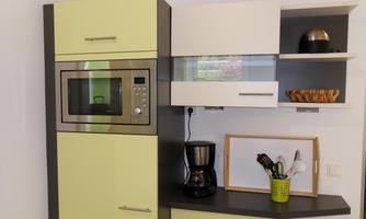 A modern kitchen with a microwave and a coffee machine. The furniture is designed in shades of green and gray.
