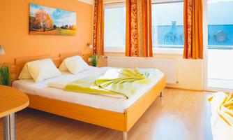 An inviting bedroom with a large bed and colorful curtains. The walls are painted orange, and a picture with a landscape motif hangs above it.