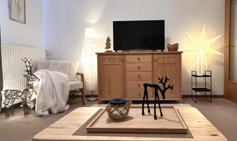A cozy living room with a television and wooden furniture. There are decorative elements such as a table, a lamp, and a small chair.