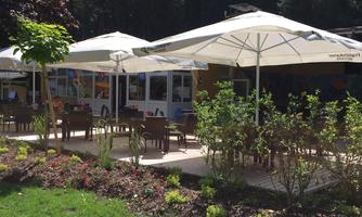A cozy outdoor area with umbrellas and seating. Surrounded by green plants and trees, it is an inviting place to relax.