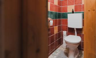 A small bathroom with a toilet and colored tiles on the walls. The fixtures are simple and functional.