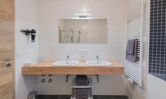 A modern bathroom with two sinks and a large mirror. The walls are brightly tiled, and there are towels and a towel warmer.