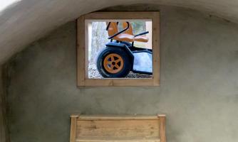 A simple room with gray walls and a wooden staircase. Through a window, one can see an orange vehicle.