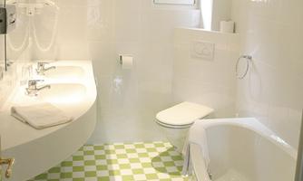 A modern bathroom with white walls and green and white tiles. There is a bathtub, a sink, and a toilet.