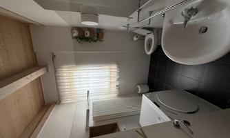 A modern bathroom with a washing machine and a sink. There are windows with curtains and a toilet area.
