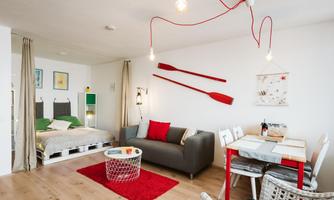 A modern and stylishly furnished apartment with a cozy sleeping area and a living room. Red accents and wooden details create an inviting atmosphere.