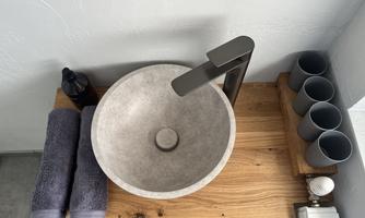 A modern concrete sink on a wooden table. Next to the sink are two towels and several gray cups.