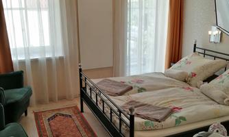 Bedroom with a bed, two armchairs and a carpet. Large windows provide plenty of natural light.