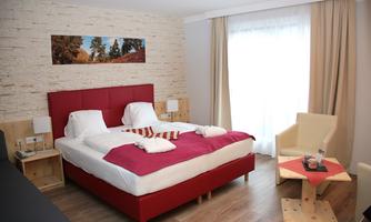 A modern hotel room with a large bed and a cozy seating area. It also features a bright window area and decorative elements on the wall.