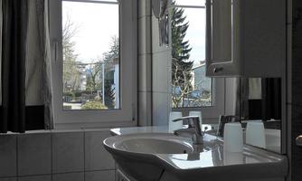 A bright bathroom with a modern sink area. Large windows let in plenty of daylight and offer a view of the outdoors.