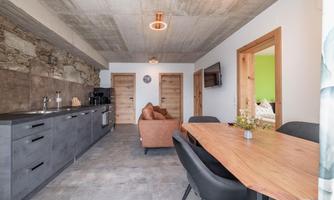 A modern kitchen with a dining area and a cozy living room. The walls are in neutral tones, and there are natural wooden elements.