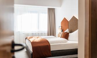 A modern hotel room with two beds and cozy furnishings. Large window area with natural light.