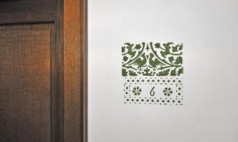 A decorative wall design with a green pattern and the number 6. The wall is light and has a wooden frame door next to it.