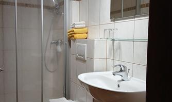 A modern bathroom with a shower, sink, and toilet. Towels are neatly placed on a shelf.