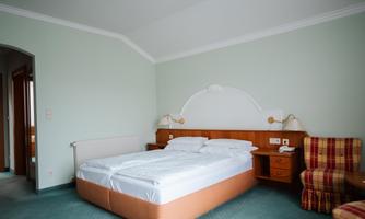A simple and cozy hotel room with a double bed and an armchair. The walls are painted in soft colors and the floor is carpeted.