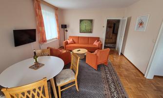 A cozy living room with orange furniture and a round table. The room has large windows that let in plenty of natural light.