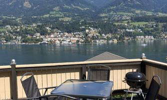 A beautiful view of a lake surrounded by mountains. On a terrace, there are a table and chairs, perfect for relaxing outdoors.