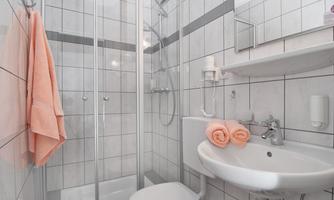A modern bathroom with a glass shower and white tiles. There is a sink with towels and a toilet area.